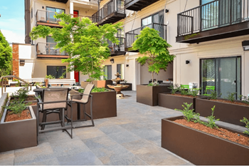 A patio with chairs and planters is surrounded by apartment buildings.